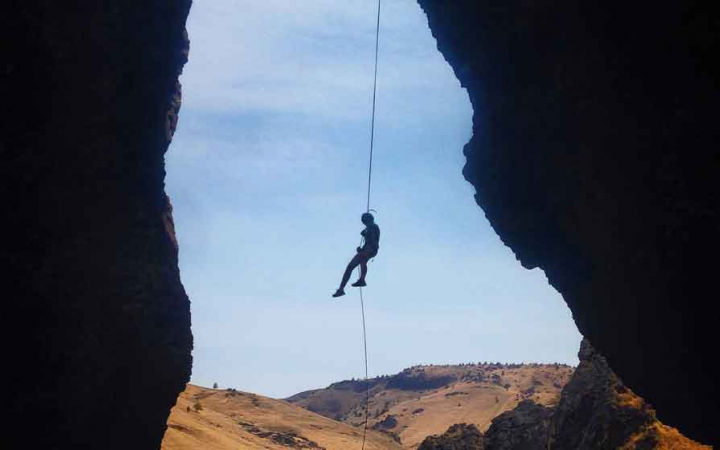 the silhouette of a rock climber on a rope rests between two rock walls while rappelling 